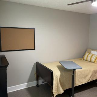 A minimalist bedroom with a bed, small desk, and an empty corkboard on the wall.