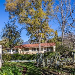 A picturesque house surrounded by lush greenery and tall trees under a clear blue sky.