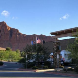 A building surrounded by trees with flags in front, set against a backdrop of mountains under a clear blue sky.