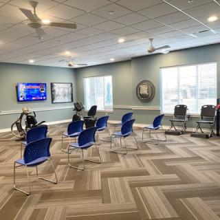 A modern conference room with blue chairs and a TV screen, featuring large windows for natural light.