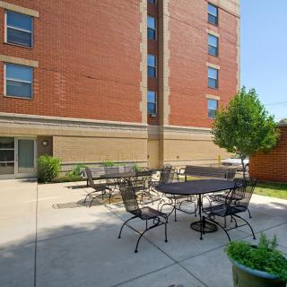 A sunny outdoor patio with tables and chairs next to a brick apartment building.