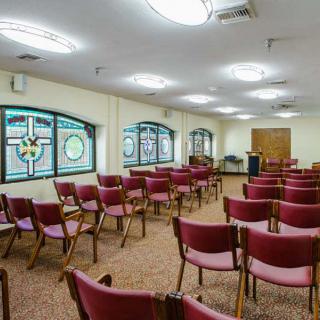An empty room with rows of chairs and decorative stained glass windows.