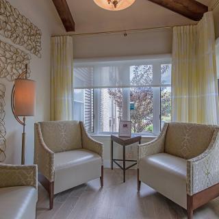 A cozy living room with neutral-colored chairs, a window with curtains, and a decorative wall.