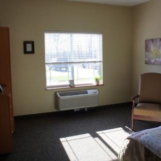 A minimalist room with a bed, chair, and a window letting in natural light.