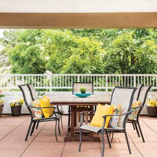 A serene patio setup with a wooden table and comfortable chairs surrounded by lush greenery.