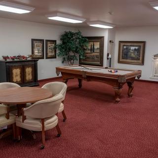 A well-furnished game room with a billiards table and seating area, adorned with artwork on the walls.
