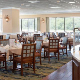 A spacious restaurant dining area with neatly arranged tables and chairs, surrounded by large windows.
