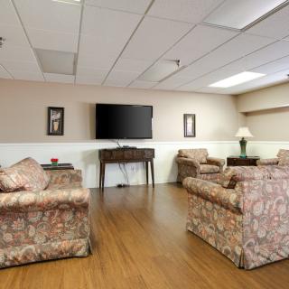A cozy living room with floral-patterned sofas, a television mounted on the wall, and a wooden floor.