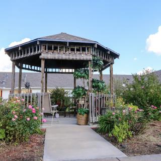 A wooden gazebo surrounded by a vibrant garden with a paved pathway leading to it.