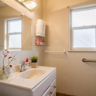 A well-lit bathroom with a white sink, a large mirror, and a window providing natural light.