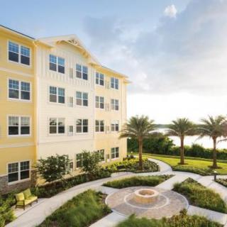 A modern apartment building surrounded by a landscaped garden with palm trees and a pathway.