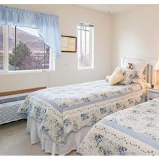 A cozy bedroom with two twin beds covered in floral bedding, featuring a large window with blue curtains.