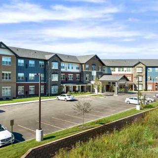A modern three-story residential building with a spacious parking lot under a partly cloudy sky.