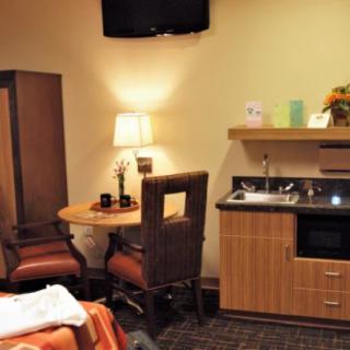 A cozy hospital room with a bed, table and chairs, television, and a small kitchenette area.