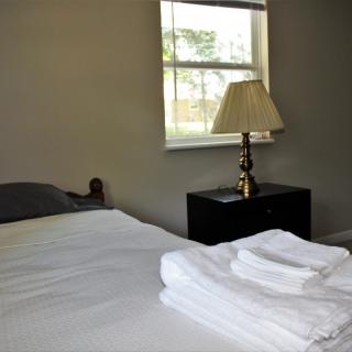 A neatly made bed with folded towels next to a lamp by the window in a bedroom.