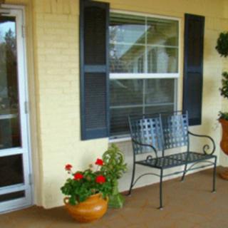 A cozy porch with a bench, potted plant, and window with shutters.