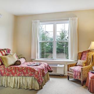 A cozy bedroom with a bed and chair by a large window, decorated in warm tones.