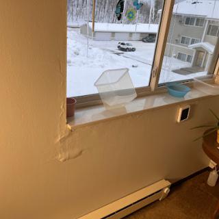 A cozy apartment window view with snow outside, featuring a simple interior and hints of winter decor.