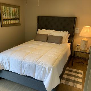 A cozy bedroom with a neatly made bed, featuring neutral tones and soft lighting.