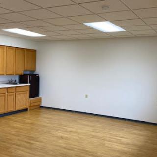 An empty office space with a kitchenette and wooden flooring.