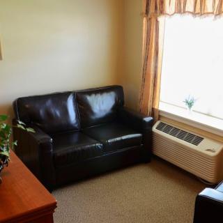 A cozy corner of a living room featuring a black leather sofa, adjacent to a window with curtains and an air conditioning unit.