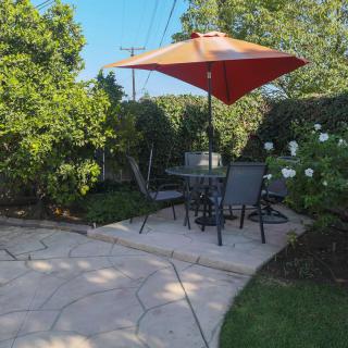 A sunny garden patio with chairs, a table, and an orange umbrella.