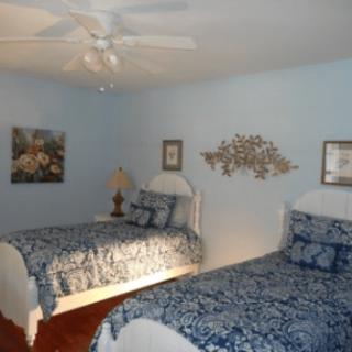 A bedroom with two twin beds featuring blue bedding, complemented by wall art and a ceiling fan.