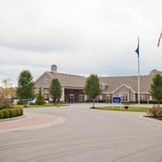 A spacious building with flags stands amidst a landscaped driveway under a cloudy sky.