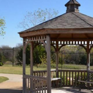 A wooden gazebo in a park setting with open skies and surrounding greenery.