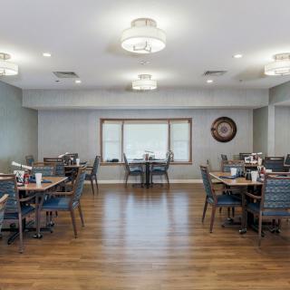 A modern dining area with neatly arranged tables and chairs, featuring elegant lighting and wooden flooring.
