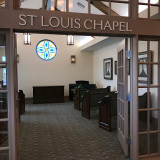 Interior view of St. Louis Chapel featuring wooden pews and a decorative window.