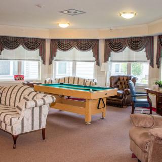 A cozy living room with a pool table, sofas, and large windows adorned with curtains.