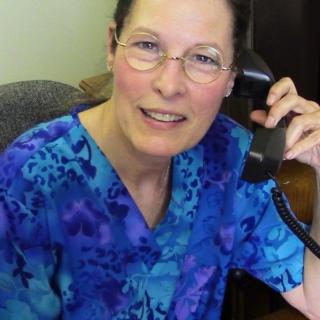 A person wearing glasses and a blue shirt is smiling while talking on the phone in an office setting.
