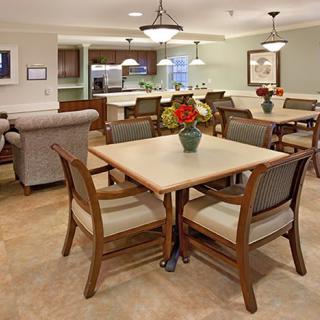 A cozy dining area with a table set and chairs, featuring warm lighting and a view into the kitchen.