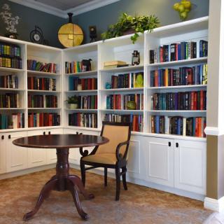 A cozy library corner featuring a round table and chair surrounded by white bookshelves filled with books.