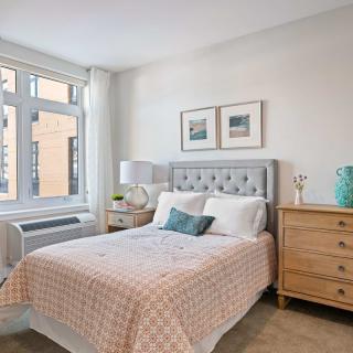 A cozy bedroom with a neatly made bed, wooden dresser, and large window.