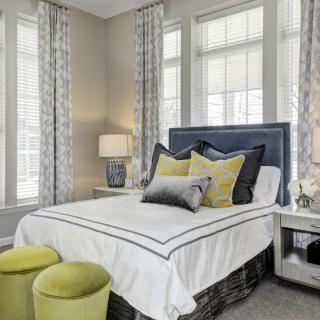 A modern bedroom with a neatly made double bed, accented with yellow and gray pillows, alongside stylish decor.