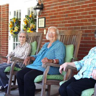 Three elderly women sitting on rocking chairs on a porch.