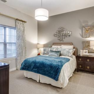 A modern bedroom interior featuring a cozy bed with blue accents, a decorative mirror on the wall, and stylish furniture.