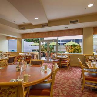 A cozy dining area with arranged tables and chairs, featuring large windows looking out to a garden.