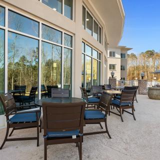 Outdoor patio area with tables and chairs beside a building with large windows.