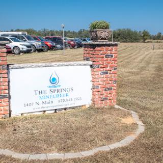 Entrance sign for The Springs, with a view of the parking area and open field.