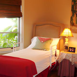 A cozy bedroom with a single bed, bedside table, and warm lighting.