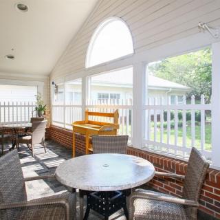 A bright patio area with outdoor seating, featuring a table and chairs surrounded by a white fence and brick walls.
