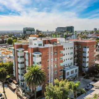 Aerial view of a modern apartment building in an urban setting with palm trees and city skyline in the background.