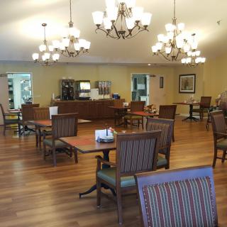 A cozy dining room with tables and chairs, warmly lit by chandeliers.