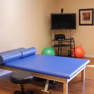 A physical therapy room equipped with a treatment table, fitness balls, and a TV screen.
