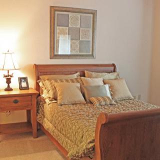 A cozy bedroom with a wooden bed and nightstand, accompanied by decorative pillows and a lamp.