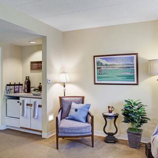 A cozy living area featuring a comfortable chair with a cushion, a side table with decorative items, and a potted plant under soft lighting.