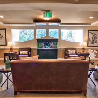 A cozy living room with a central aquarium, surrounded by sofas and natural light from the windows.